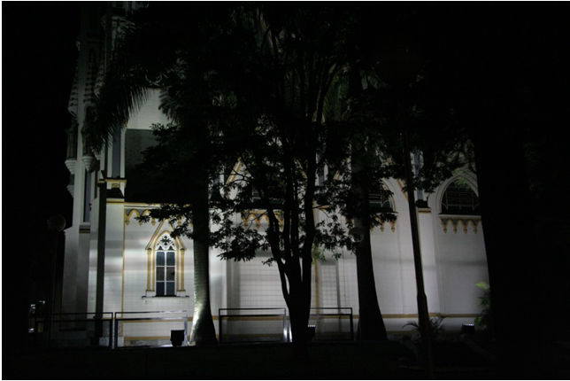 Fachada da Igreja de Lourdes iluminada, vista entre árvores