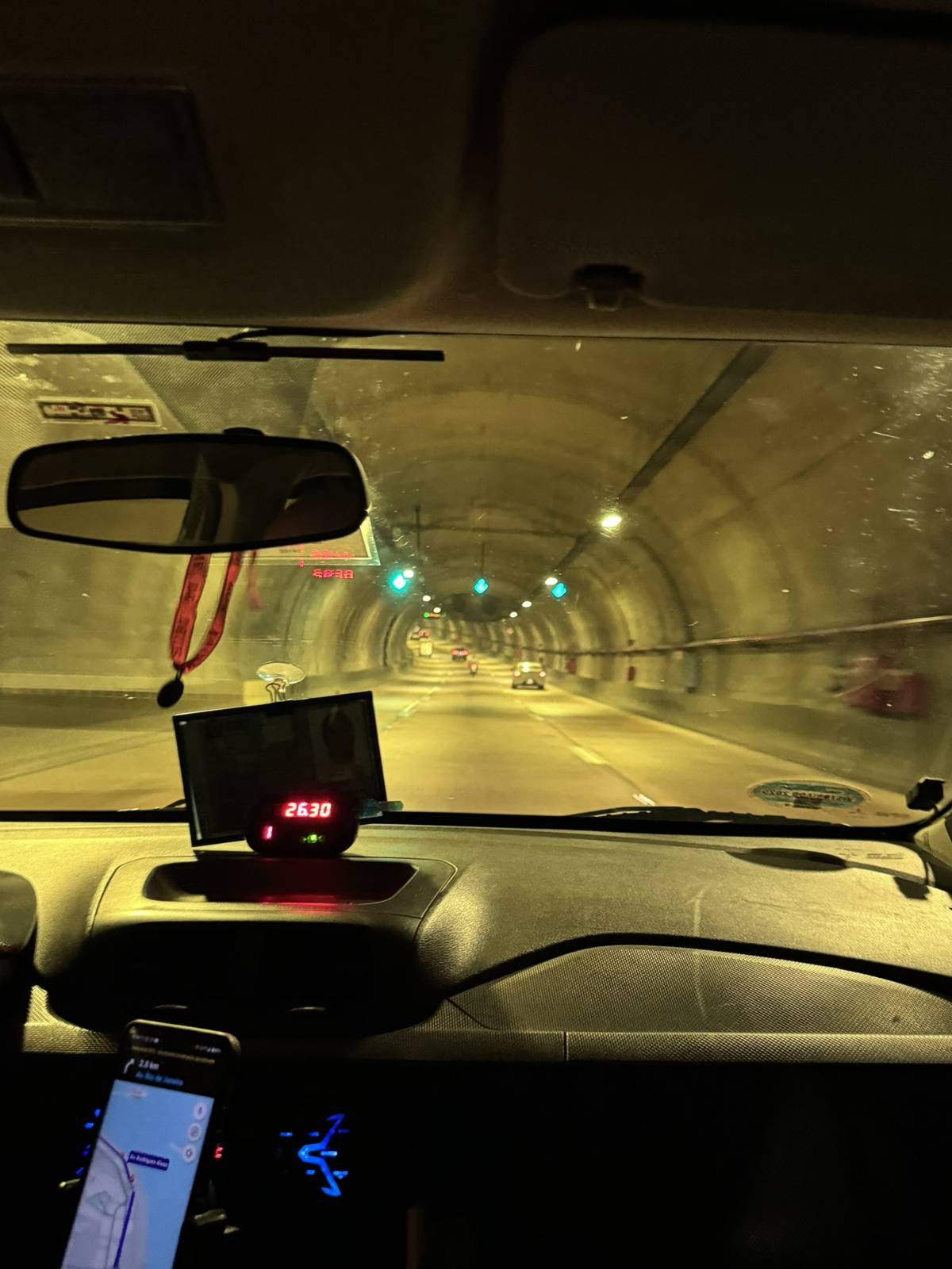Interior de túnel rodoviário visto de dentro de um veículo, com a iluminação linear do teto guiando o tráfego